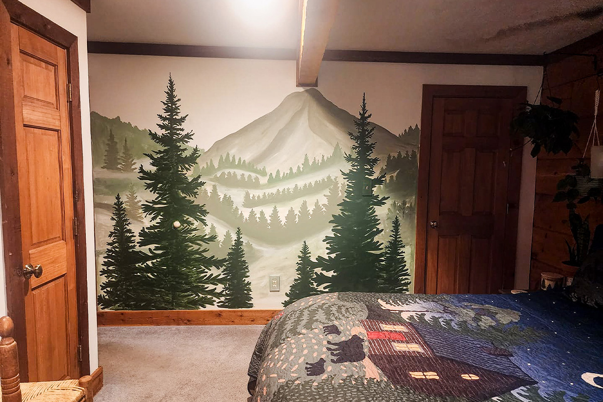 Hand-painted mountain landscape mural with trees on a bedroom wall