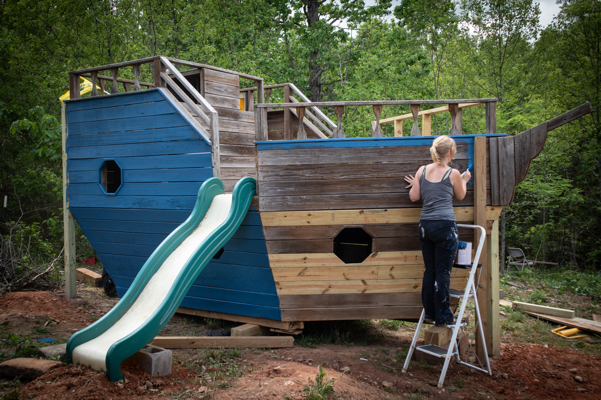 Female painter applying blue paint to a wooden outdoor play structure
